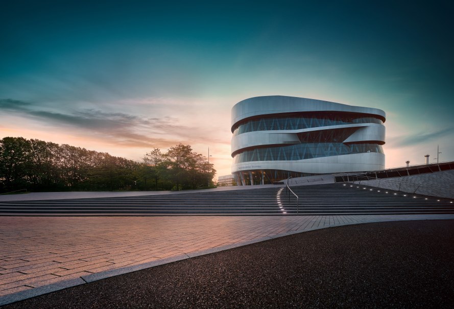 Das Mercedes-Benz Museum in Stuttgart bei Sonnenuntergang. Moderne Architektur mit geschwungenen Linien, umgeben von B&auml;umen und beleuchteten Stufen., &copy; Mercedes-Benz Heritage GmbH