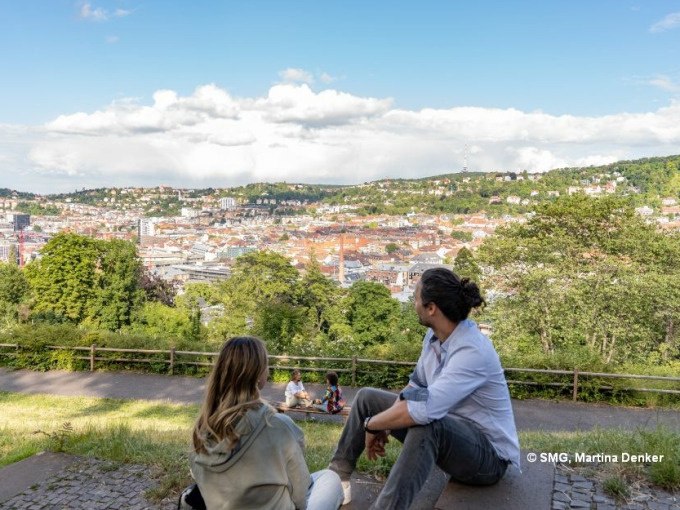 Zwei Personen sitzen auf einer Bank und genießen den Ausblick auf Stuttgart. Im Hintergrund sind grüne Hügel und die Stadtlandschaft zu sehen., © Stuttgart Marketing GmbH Zwei Personen sitzen auf einer Bank und genießen den Ausblick auf Stuttgart. Im Hintergrund sind grüne Hügel und die Stadtlandschaft zu sehen., © Stuttgart Marketing GmbH