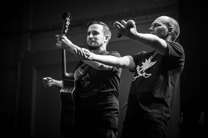 Two musicians on stage, one holding a guitar, the other a microphone. Both are wearing black T-shirts. Black and white photograph., &copy; Rosenau Kultur e.V.