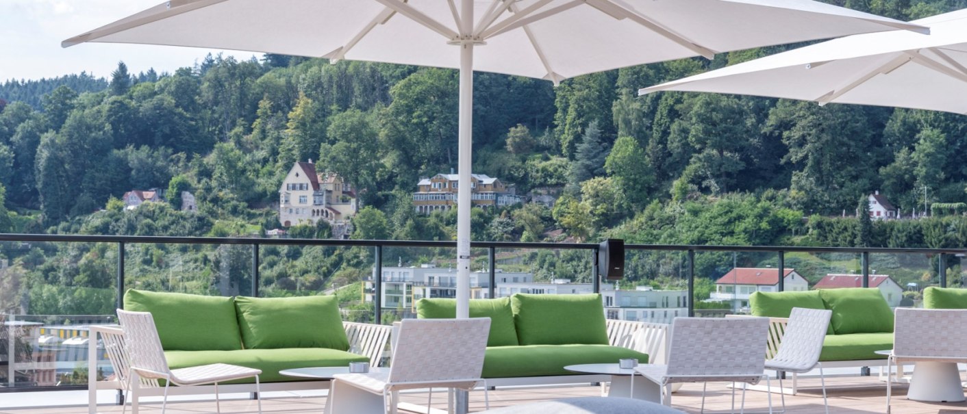 Rooftop bar with green sofas, white tables and parasols. Wooded hills and houses in the background. Relaxed atmosphere., © Hotel am Remspark Rooftop bar with green sofas, white tables and parasols. Wooded hills and houses in the background. Relaxed atmosphere., © Hotel am Remspark