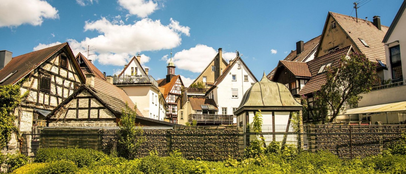 Half-timbered houses in the old town of Bad Urach, surrounded by greenery, under a clear blue sky dotted with white clouds., © SMG Stuttgart Marketing GmbH - Sarah Schmid Half-timbered houses in the old town of Bad Urach, surrounded by greenery, under a clear blue sky dotted with white clouds., © SMG Stuttgart Marketing GmbH - Sarah Schmid