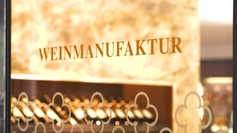 Der Eingang der Weinmanufaktur zeigt den Schriftzug auf einer Glastür. Im Hintergrund sind Weinflaschen zu sehen., © Weinmanufaktur Stuttgart Der Eingang der Weinmanufaktur zeigt den Schriftzug auf einer Glastür. Im Hintergrund sind Weinflaschen zu sehen., © Weinmanufaktur Stuttgart
