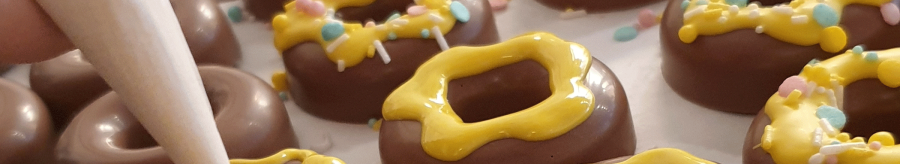 Chocolate rings are decorated with yellow icing and colorful sprinkles. One hand holds a piping bag., © kesselglueck.de Chocolate rings are decorated with yellow icing and colorful sprinkles. One hand holds a piping bag., © kesselglueck.de