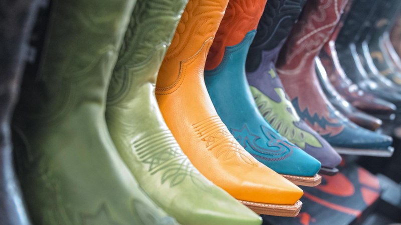 A row of colorful cowboy boots in various colors and patterns, including green, orange and blue, on display in a store., © DBoots by Boots, Stuttgart A row of colorful cowboy boots in various colors and patterns, including green, orange and blue, on display in a store., © DBoots by Boots, Stuttgart
