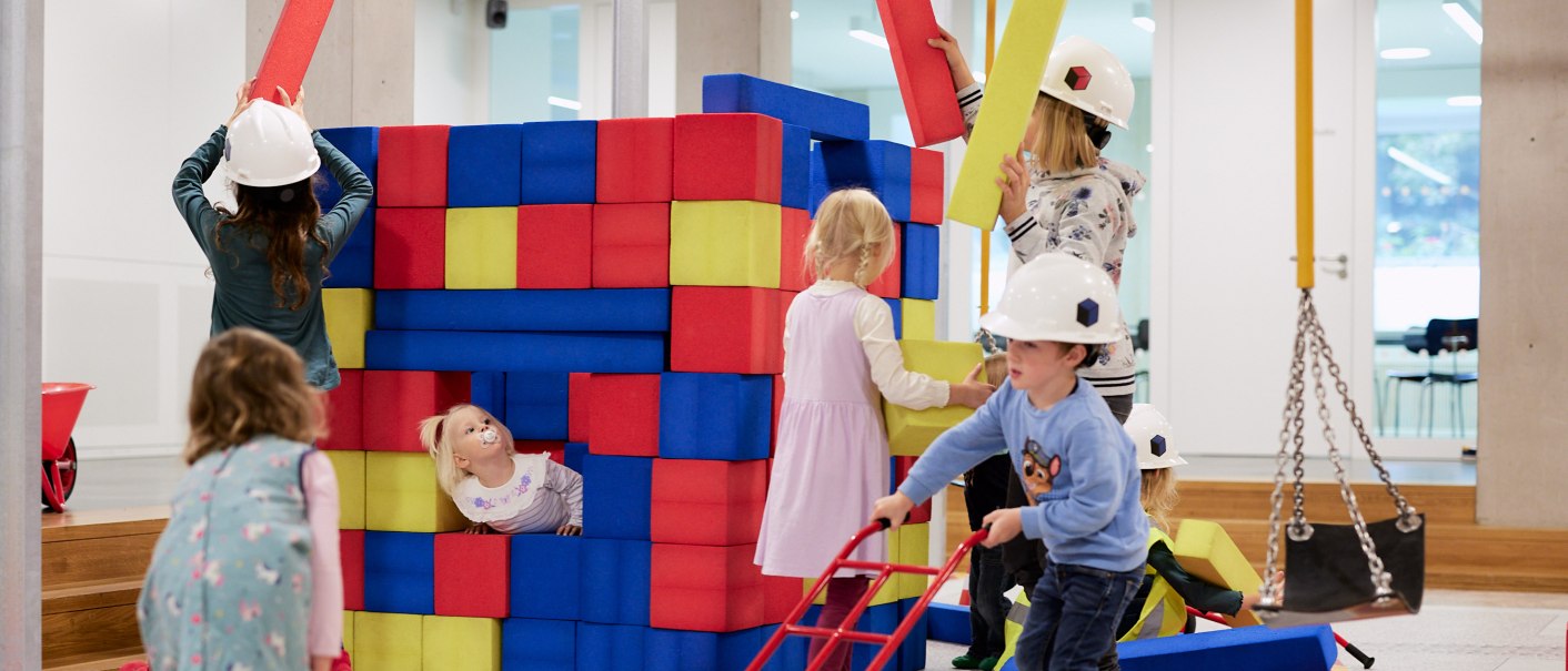Kinder spielen auf einer Indoor-Baustelle mit bunten Schaumstoffbl&ouml;cken. Sie tragen Bauhelme und haben Spa&szlig; beim Bauen und Spielen., &copy; Julia Ochs