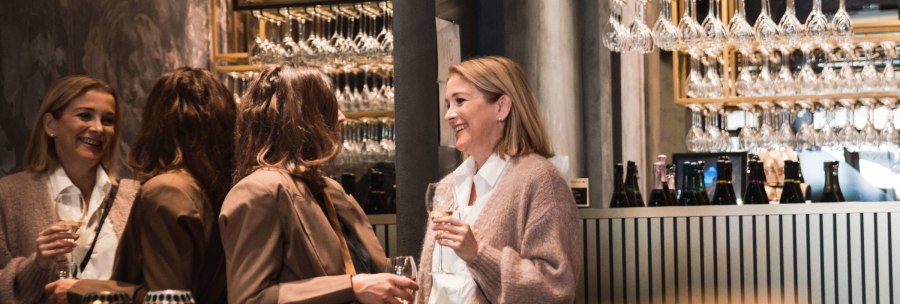 Vier Frauen unterhalten sich in einer stilvollen Bar, halten Sektgläser. Im Hintergrund hängen Gläser, Flaschen stehen auf der Theke., © Stuttgart-Marketing GmbH, wpsteinheisser