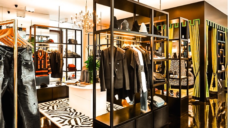 Modernes Bekleidungsgeschäft mit stilvollen Regalen, Kleidung und Accessoires. Ein Kronleuchter hängt von der Decke, der Boden ist glänzend., © Abseits Stuttgart Modernes Bekleidungsgeschäft mit stilvollen Regalen, Kleidung und Accessoires. Ein Kronleuchter hängt von der Decke, der Boden ist glänzend., © Abseits Stuttgart