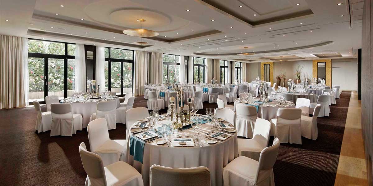 Elegant ballroom with round, white-covered tables and chairs, decorated for an event., © Parkhotel Stuttgart Messe-Airport Elegant ballroom with round, white-covered tables and chairs, decorated for an event., © Parkhotel Stuttgart Messe-Airport