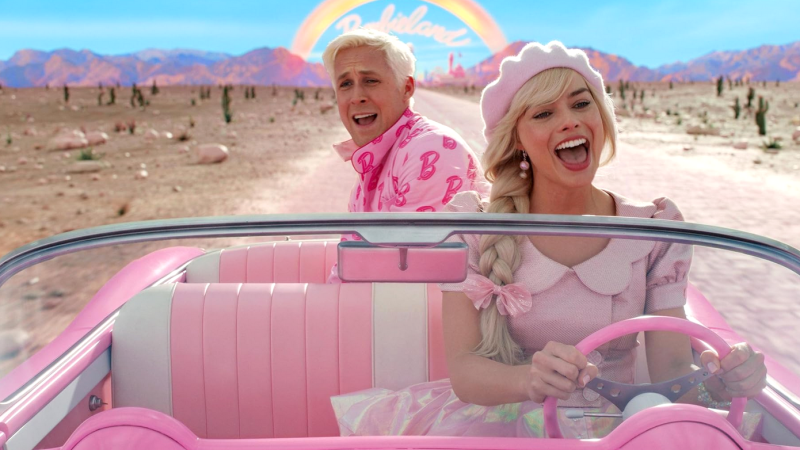 Zwei Personen in einem pinken Cabrio fahren durch eine Wüstenlandschaft. Ein Regenbogen und der Schriftzug "Barbie" sind im Hintergrund zu sehen., © Warner Bros.