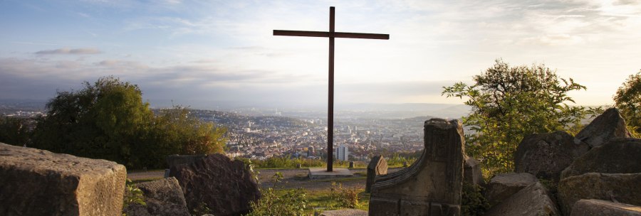 A cross on the Birkenkopf in Stuttgart, surrounded by rubble, with a view of the city in the background at sunset., © Stuttgart-Marketing GmbH, Jean-Claude Winkler A cross on the Birkenkopf in Stuttgart, surrounded by rubble, with a view of the city in the background at sunset., © Stuttgart-Marketing GmbH, Jean-Claude Winkler