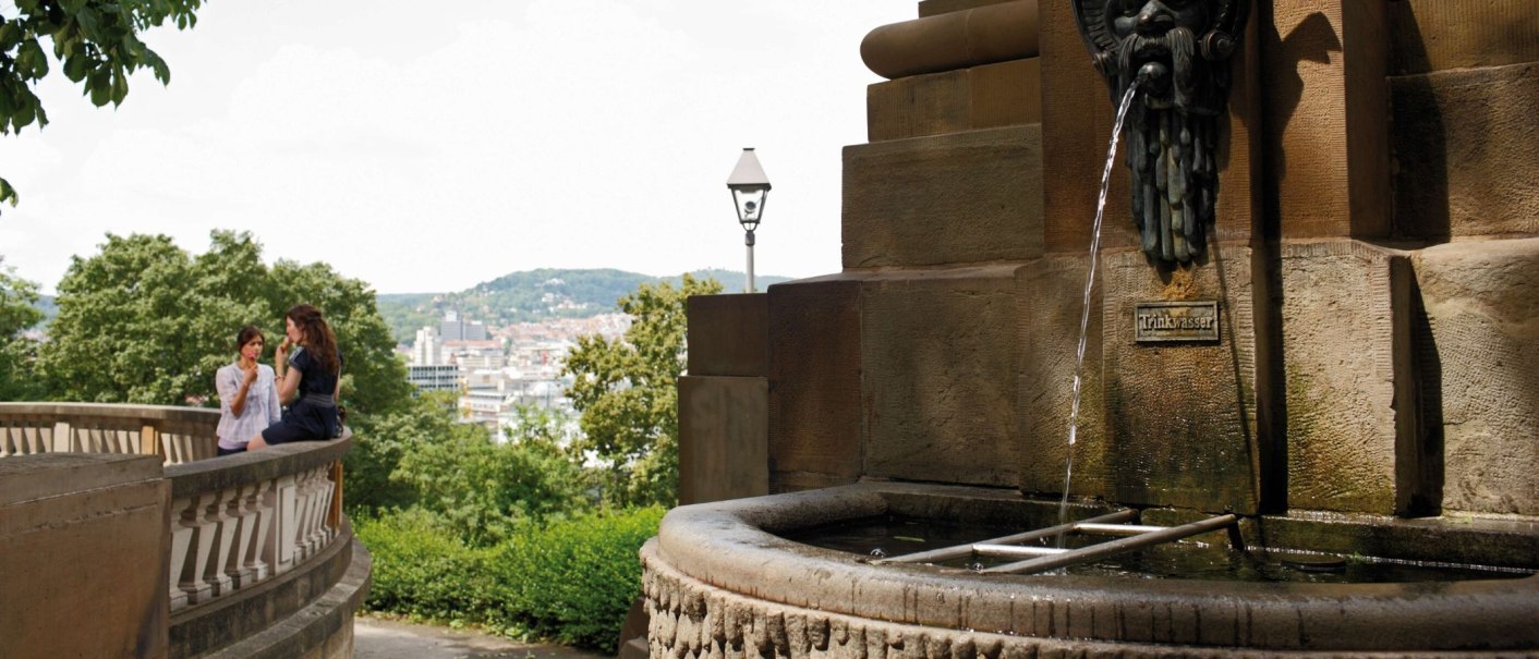 Der Galateabrunnen am Eugensplatz in Stuttgart. Zwei Personen sitzen auf einer Balustrade, im Hintergrund die Stadt und gr&uuml;ne H&uuml;gel., &copy; Stuttgart-Marketing GmbH Christoph D&uuml;pper
