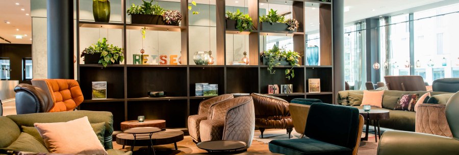 Moderne Lobby mit bequemen Sesseln, Sofas und Tischen. Regale mit Pflanzen und Dekorationen, helle Beleuchtung und gro&szlig;e Fenster., &copy; Motel One - Stuttgart Hauptbahnhof