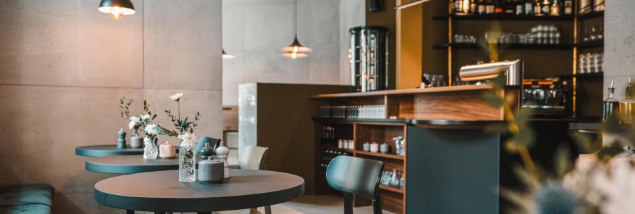 Modernes Caf&eacute; mit eleganter Einrichtung, runden Tischen und Blumenvasen. Dezente Beleuchtung und eine gut ausgestattete Bar im Hintergrund., &copy; Lupin, Stuttgart