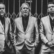 Drei Männer in eleganten Anzügen posieren ernst vor einem Gittertor. Das Bild ist in Schwarz-Weiß gehalten., © links im Bild Drei Männer in eleganten Anzügen posieren ernst vor einem Gittertor. Das Bild ist in Schwarz-Weiß gehalten., © links im Bild