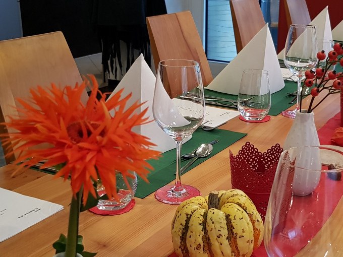 Ein festlich gedeckter Tisch mit orangefarbener Blume, Weingl&auml;sern, gefalteten Servietten und K&uuml;rbisdekoration., &copy; Kultweine-Kochwelten-Kunst&uuml;cke - Kochschule Sonja Lenz