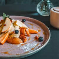 Ein Teller mit geschnittenen Früchten, Beeren und Sirup. Daneben eine Zuckerdose und ein Salzstreuer auf einem dunklen Tisch., © Lupin, Stuttgart Ein Teller mit geschnittenen Früchten, Beeren und Sirup. Daneben eine Zuckerdose und ein Salzstreuer auf einem dunklen Tisch., © Lupin, Stuttgart