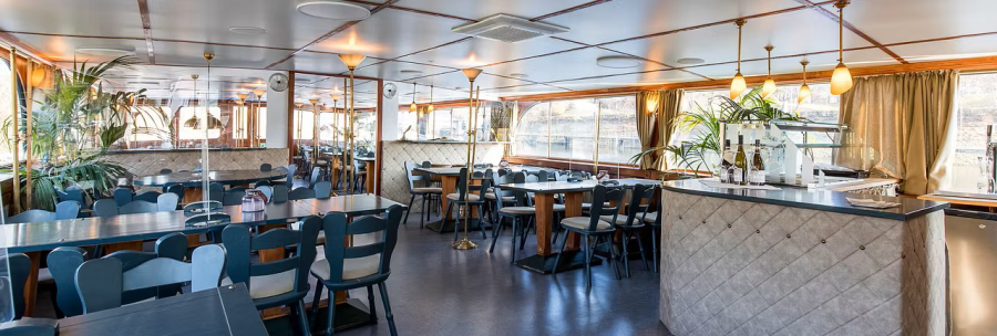 An elegant ship restaurant with covered tables, blue chairs and a bar. Large windows offer a view of the water., &copy; NeckarFlair MS Wilhelma Betriebsgesellschaft mbH
