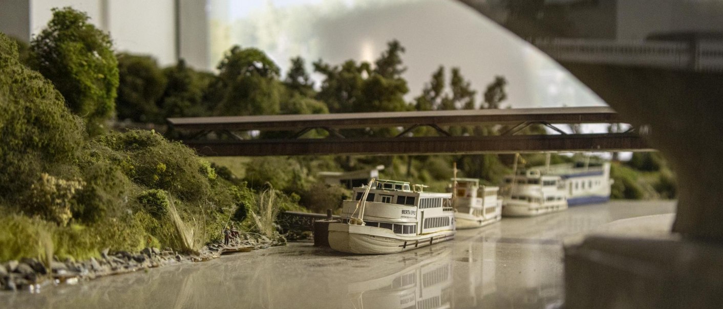 Miniature model of a river landscape with bridge, trees and several boats. Detailed presentation in an exhibition., © Stuttgart-Marketing GmbH, Sarah Schmid Miniature model of a river landscape with bridge, trees and several boats. Detailed presentation in an exhibition., © Stuttgart-Marketing GmbH, Sarah Schmid