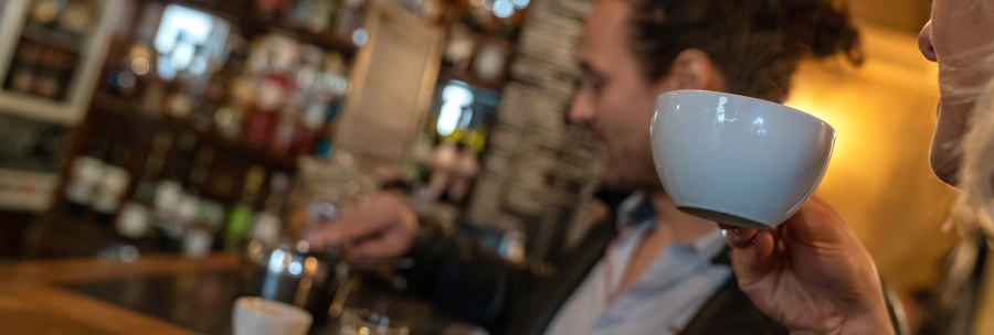 Two people in a caf&eacute;. One person is drinking from a cup while the other prepares coffee. Shelves with bottles can be seen in the background., &copy; Stuttgart Marketing  GmbH, Fotografin Martina Denker, post@denkerfotografie.de