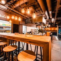 Modernes Café mit Holztischen, Hockern und hängenden Glühbirnen. Getränkekühlschrank und Menütafel im Hintergrund. Gemütliche Atmosphäre., © Andreas Dalferth Modernes Café mit Holztischen, Hockern und hängenden Glühbirnen. Getränkekühlschrank und Menütafel im Hintergrund. Gemütliche Atmosphäre., © Andreas Dalferth