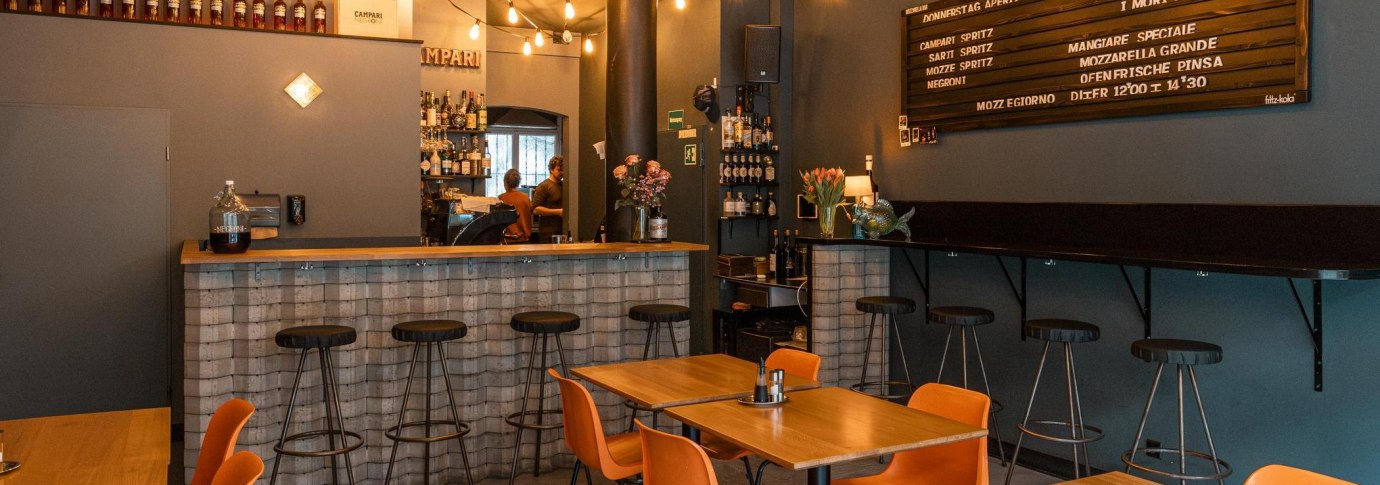 Gem&uuml;tliche Bar mit Holztischen, Barhockern und einer Theke. Lichterketten und ein Men&uuml;brett schm&uuml;cken die Wand., &copy; SMG, Sarah Schmid