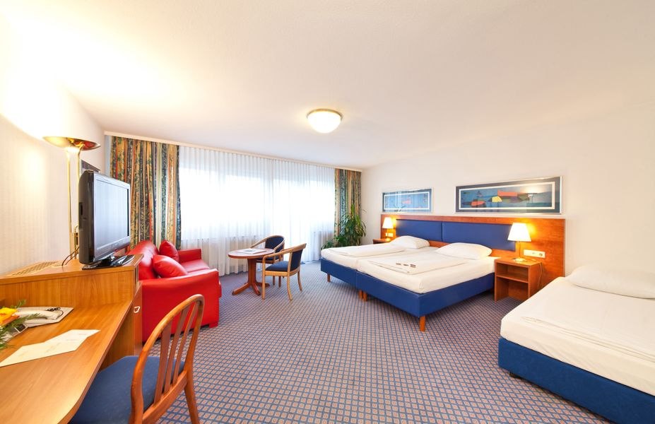 Geräumiges Hotelzimmer mit zwei Betten, rotem Sofa, Schreibtisch, Fernseher und großem Fenster mit Vorhängen., © Novum Boulevard Stuttgart City Geräumiges Hotelzimmer mit zwei Betten, rotem Sofa, Schreibtisch, Fernseher und großem Fenster mit Vorhängen., © Novum Boulevard Stuttgart City