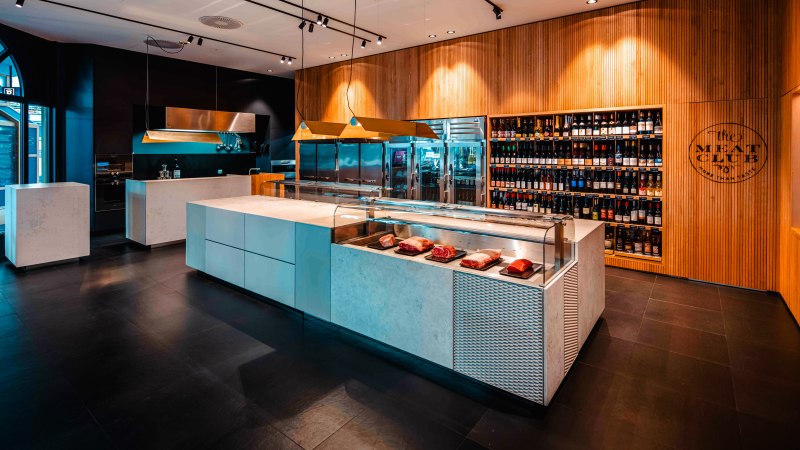 Modernes Fleischgeschäft mit eleganter Theke, Fleischpräsentation und großem Weinregal an der Wand. Stilvolle Beleuchtung und Holzverkleidung., © The Meat Club, Stuttgart Modernes Fleischgeschäft mit eleganter Theke, Fleischpräsentation und großem Weinregal an der Wand. Stilvolle Beleuchtung und Holzverkleidung., © The Meat Club, Stuttgart