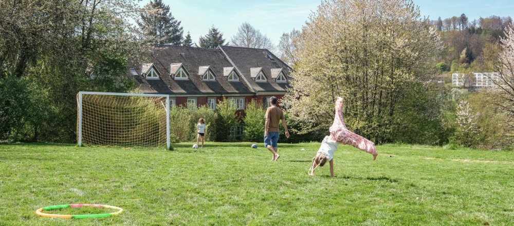 Kinder spielen auf einem gr&uuml;nen Fu&szlig;ballplatz mit einem Tor, umgeben von B&auml;umen und einem Haus im Hintergrund., &copy; DJH Baden-W&uuml;rttemberg e.V.