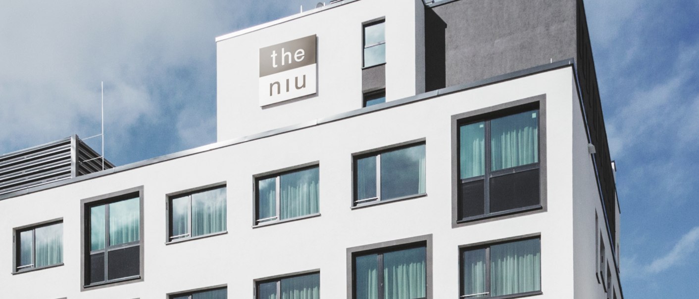 A modern hotel exterior with large windows and the "the niu" logo on the top floor., © the niu Form - Novum Hospitality A modern hotel exterior with large windows and the "the niu" logo on the top floor., © the niu Form - Novum Hospitality