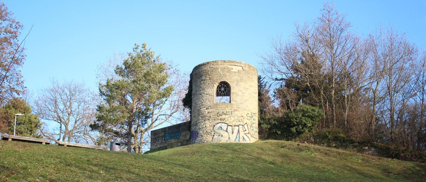 Eine alte, runde Ruine mit Graffiti steht auf einem grasbewachsenen Hügel, umgeben von kahlen Bäumen und blauem Himmel., © SMG