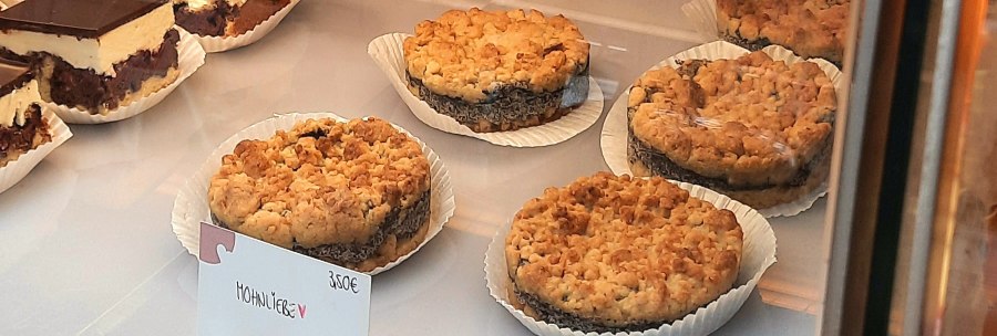 Poppy seed cake and chocolate cake are displayed in a showcase. A sign shows the price of €3.50 for the poppy seed cake., © SMG