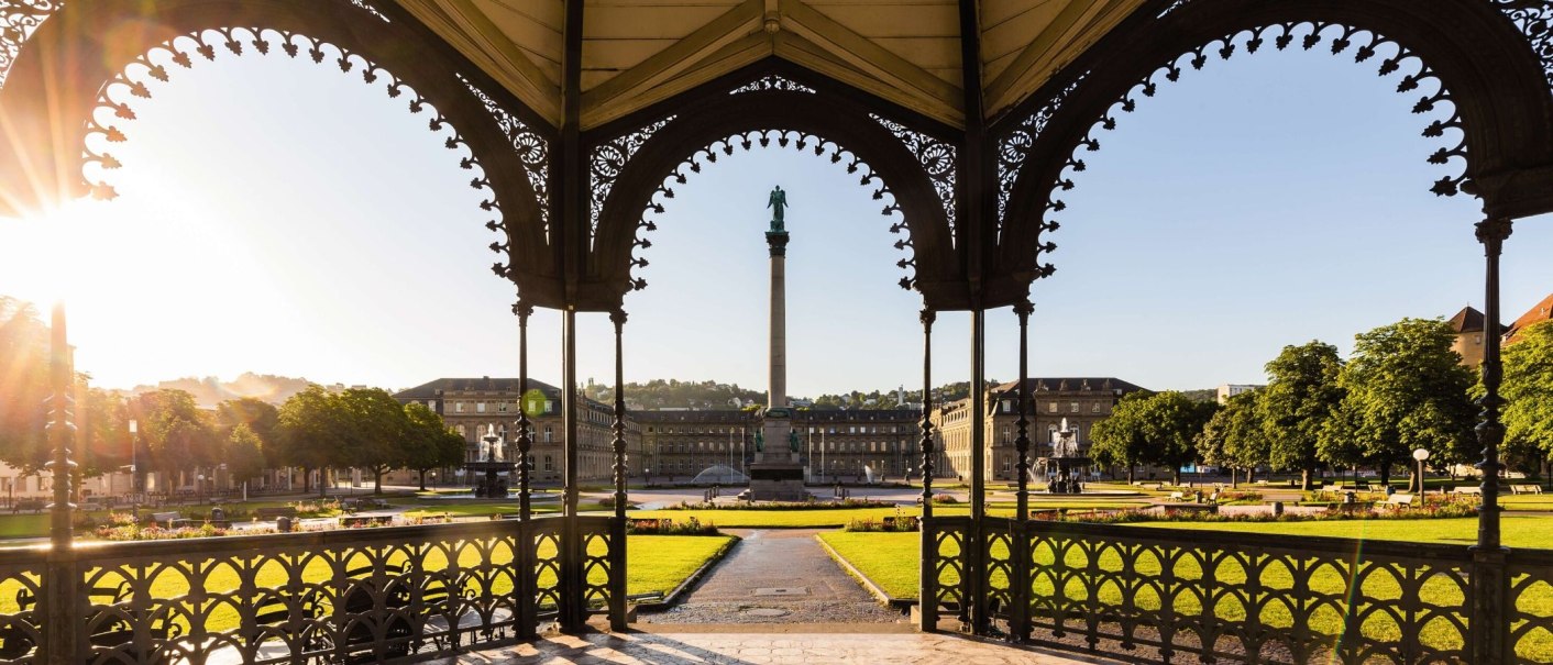 Blick durch einen Pavillon auf den Schlossplatz Stuttgart mit der Jubil&auml;umss&auml;ule, umgeben von historischen Geb&auml;uden und gr&uuml;nen Rasenfl&auml;chen im Sonnenlicht., &copy; Stuttgart-Marketing GmbH Werner Dieterich