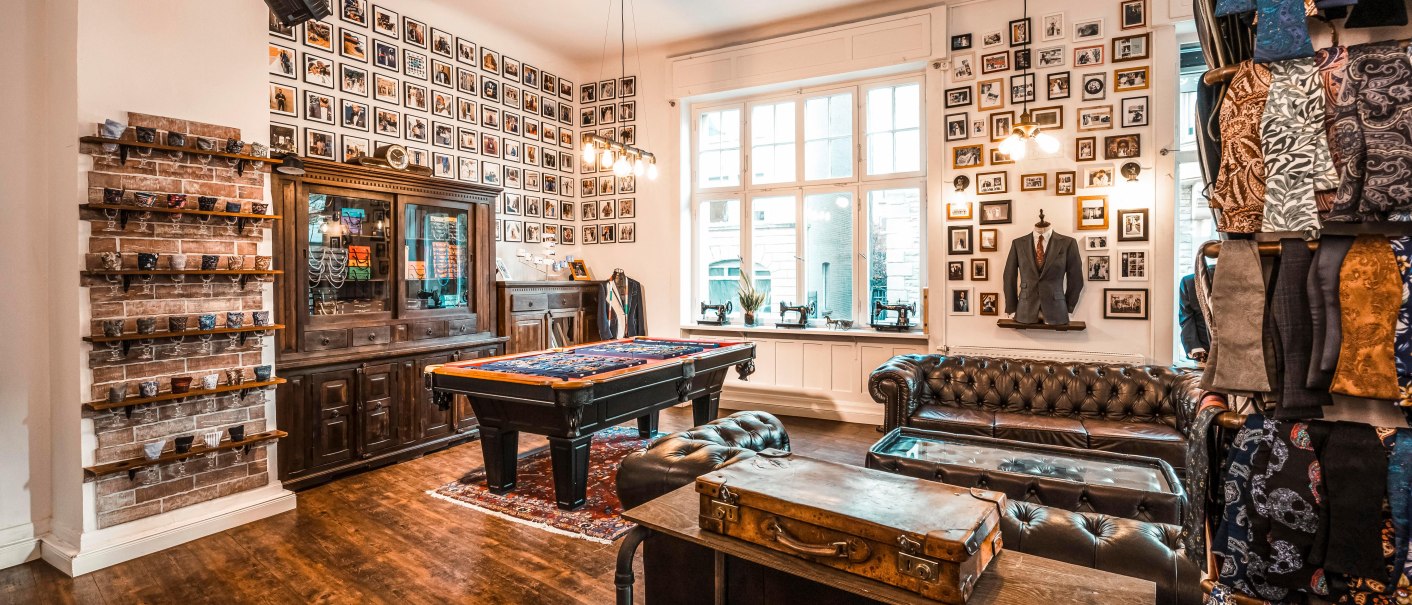 Ein stilvoller Verkaufsraum mit Ledersofas, einem Billardtisch, Vintage-Dekor und Stoffmustern an den Wänden., © Mr. Ash Tailor Store, Stuttgart