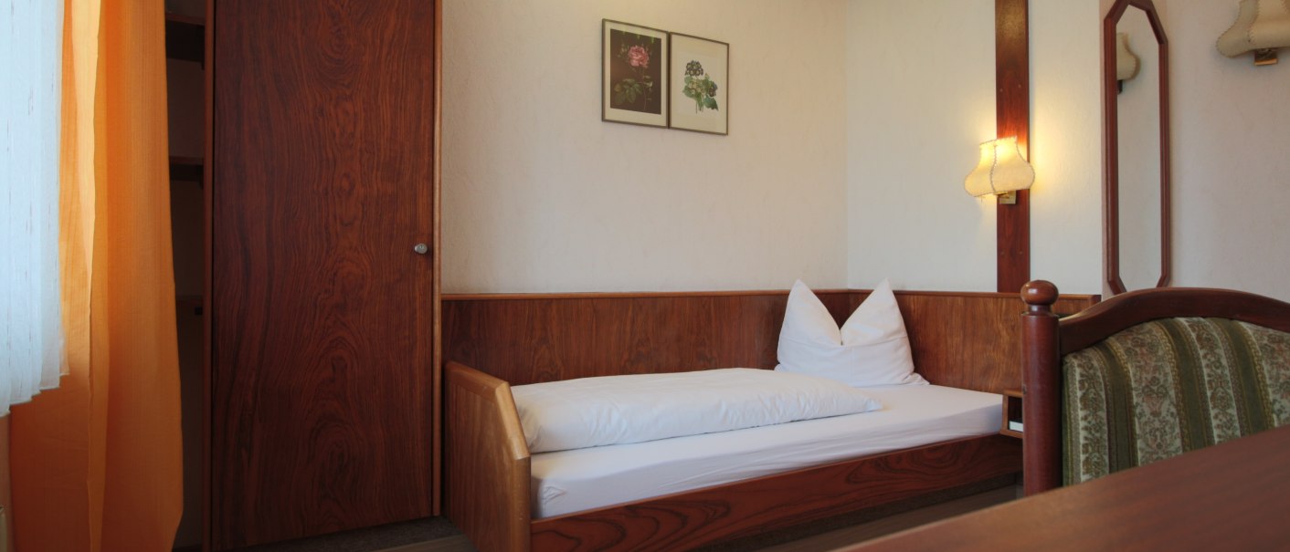 A cozy single room with wooden furniture, a single bed, two murals and a lamp. A mirror and orange curtains are also visible., © TOMAS A cozy single room with wooden furniture, a single bed, two murals and a lamp. A mirror and orange curtains are also visible., © TOMAS