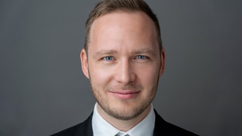 Ein Mann in einem Anzug lächelt in die Kamera. Der Hintergrund ist grau., © Renitenztheater Stuttgart e.V.