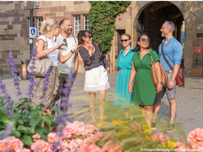 Eine Gruppe von Menschen steht lachend vor einem historischen Gebäude in Stuttgart, umgeben von Blumen und sommerlicher Kleidung., © Stuttgart Marketing GmbH Eine Gruppe von Menschen steht lachend vor einem historischen Gebäude in Stuttgart, umgeben von Blumen und sommerlicher Kleidung., © Stuttgart Marketing GmbH