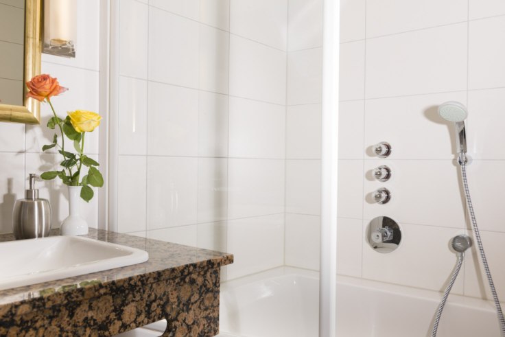 Modernes Badezimmer mit weißer Fliesenwand, Duscharmatur, Waschbecken mit Granitplatte und Vase mit Rosen., © Hotel Adler Waiblingen Modernes Badezimmer mit weißer Fliesenwand, Duscharmatur, Waschbecken mit Granitplatte und Vase mit Rosen., © Hotel Adler Waiblingen