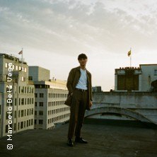 Eine Person steht auf einem Dach, umgeben von städtischen Gebäuden bei Sonnenuntergang. Der Himmel ist leicht bewölkt., © links im Bild Eine Person steht auf einem Dach, umgeben von städtischen Gebäuden bei Sonnenuntergang. Der Himmel ist leicht bewölkt., © links im Bild