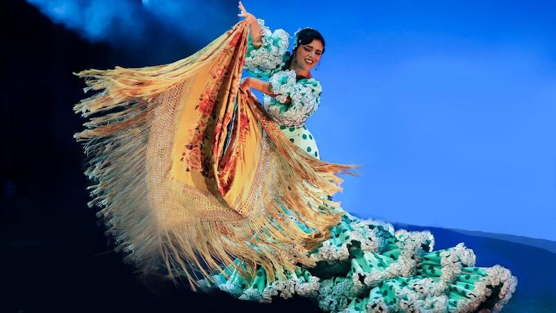 Eine Flamenco-T&auml;nzerin in einem gr&uuml;nen Kleid mit wei&szlig;en Punkten und Fransen tanzt leidenschaftlich auf einer B&uuml;hne mit blauem Hintergrund., &copy; Stuttgarter Flamenco Festival gUG