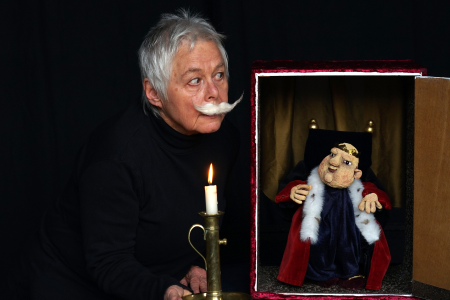 Eine Person mit falschem Schnurrbart hält eine Kerze neben einer königlichen Puppe in einem kleinen Theaterkasten., © Theater in der Badewanne Eine Person mit falschem Schnurrbart hält eine Kerze neben einer königlichen Puppe in einem kleinen Theaterkasten., © Theater in der Badewanne