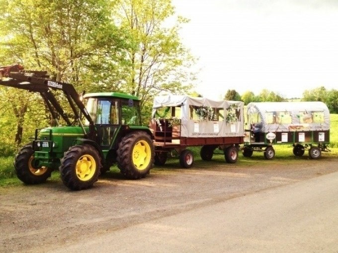 A green tractor pulls two trailers with canopies, ideal for group outings in rural surroundings., © Cool-Tours StattReisen A green tractor pulls two trailers with canopies, ideal for group outings in rural surroundings., © Cool-Tours StattReisen