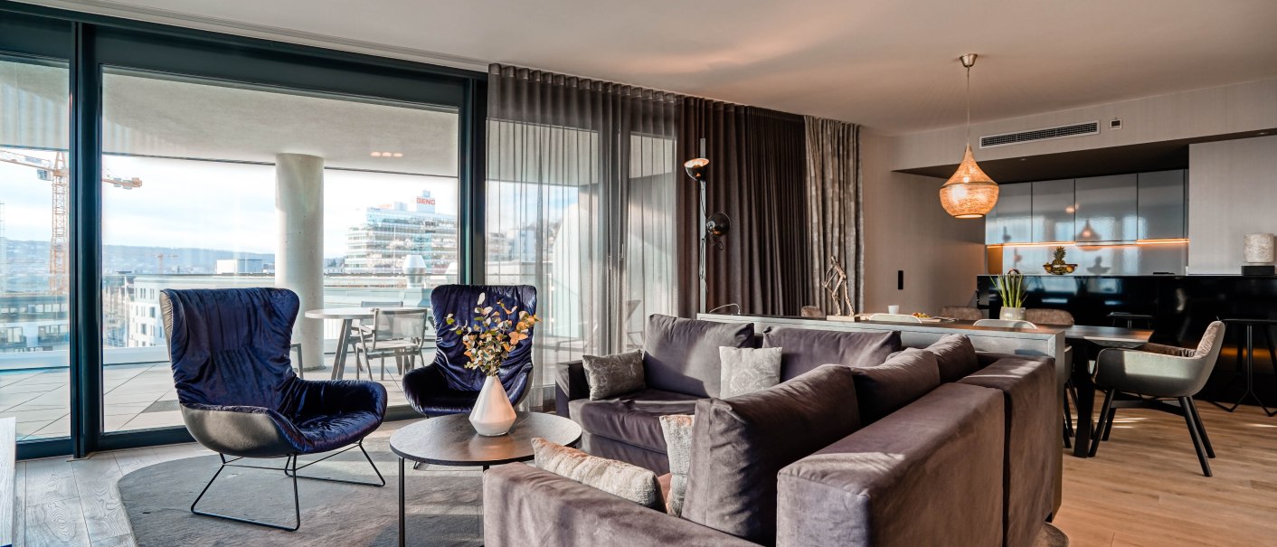 Elegante Suite mit modernen Möbeln, großen Fenstern und Balkon. Stilvolle Einrichtung mit Sofas, Sesseln und Esstisch. Helle, einladende Atmosphäre., © CLOUD N°7 APARTMENTS GmbH