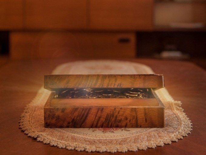 Eine geöffnete Holzkiste mit glänzenden Münzen steht auf einem bestickten Tischläufer in einem warm beleuchteten Raum., © ExitGames Stuttgart Eine geöffnete Holzkiste mit glänzenden Münzen steht auf einem bestickten Tischläufer in einem warm beleuchteten Raum., © ExitGames Stuttgart