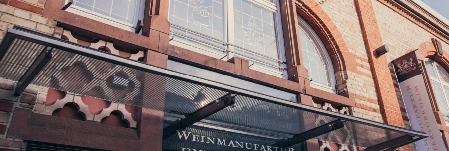 Fassade der Weinmanufaktur Untertürkheim mit Glasvordach, Schriftzug und dekorativen Fenstern., © Weinmanufaktur Stuttgart Fassade der Weinmanufaktur Untertürkheim mit Glasvordach, Schriftzug und dekorativen Fenstern., © Weinmanufaktur Stuttgart