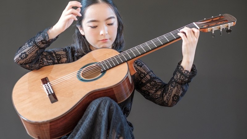 Eine Frau in schwarzer Spitzenkleidung spielt konzentriert auf einer klassischen Gitarre vor einem neutralen Hintergrund., © Staatliche Hochschule für Musik und Darstellende Kunst Eine Frau in schwarzer Spitzenkleidung spielt konzentriert auf einer klassischen Gitarre vor einem neutralen Hintergrund., © Staatliche Hochschule für Musik und Darstellende Kunst