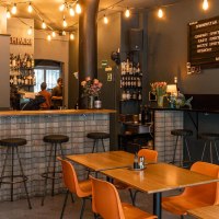 Gemütliche Bar mit Holztischen, Barhockern und einer Theke. Lichterketten und ein Menübrett schmücken die Wand., © SMG, Sarah Schmid Gemütliche Bar mit Holztischen, Barhockern und einer Theke. Lichterketten und ein Menübrett schmücken die Wand., © SMG, Sarah Schmid