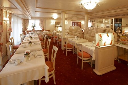 An elegant breakfast room with white tablecloths, red chairs, and decorative lighting. A buffet area is visible in the background., © Jeanette Bender An elegant breakfast room with white tablecloths, red chairs, and decorative lighting. A buffet area is visible in the background., © Jeanette Bender