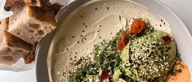 Ein Teller mit Avocado, Sprossen, Tomaten und Sesam, daneben liegt frisches Brot., © wyld Stuttgart Ein Teller mit Avocado, Sprossen, Tomaten und Sesam, daneben liegt frisches Brot., © wyld Stuttgart