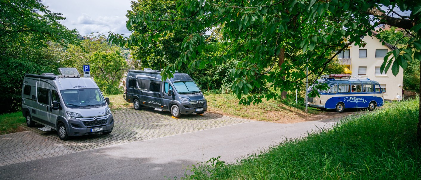 Wohnmobilstellplatz in Esslingen mit drei geparkten Fahrzeugen unter Bäumen. Ein blau-weißer Bus und zwei Wohnmobile stehen auf gepflastertem Boden., © Stuttgart-Marketing GmbH, Thomas Niedermüller Wohnmobilstellplatz in Esslingen mit drei geparkten Fahrzeugen unter Bäumen. Ein blau-weißer Bus und zwei Wohnmobile stehen auf gepflastertem Boden., © Stuttgart-Marketing GmbH, Thomas Niedermüller