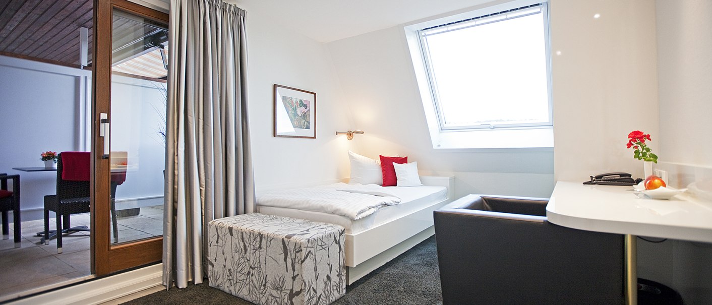 Helles Einzelzimmer mit Bett, Balkonzugang, Schreibtisch und Dachfenster. Moderne Einrichtung mit roten Akzenten und gem&uuml;tlicher Atmosph&auml;re., &copy; Hotel Krone